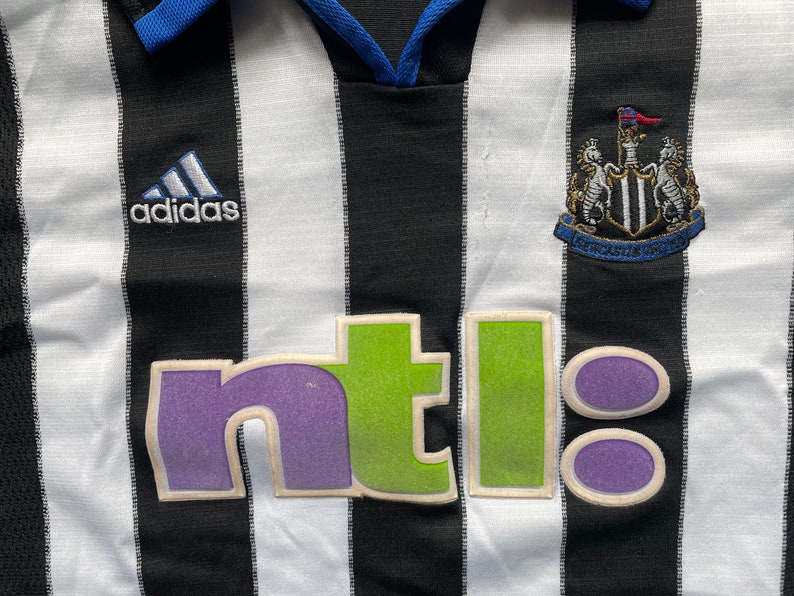 May include: Black and white striped football shirt with a blue collar and the Adidas logo on the left breast. The shirt has a green and purple "ntl" logo on the front and the Newcastle United crest on the right breast.