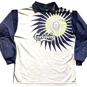 May include: White long-sleeve soccer jersey with a blue and white swirl design. The jersey has a blue collar and blue sleeves with padded elbows. The Carlsberg logo is printed on the front of the jersey.