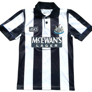 K&ouml;nnte beinhalten: Schwarz-wei&szlig; gestreiftes Fu&szlig;balltrikot mit schwarzem Kragen und &Auml;rmeln. Das Trikot zeigt das "Asics"-Logo, das "McEwan's Lager"-Logo und ein Teamwappen. Die &Auml;rmel haben blaue Paspeln.