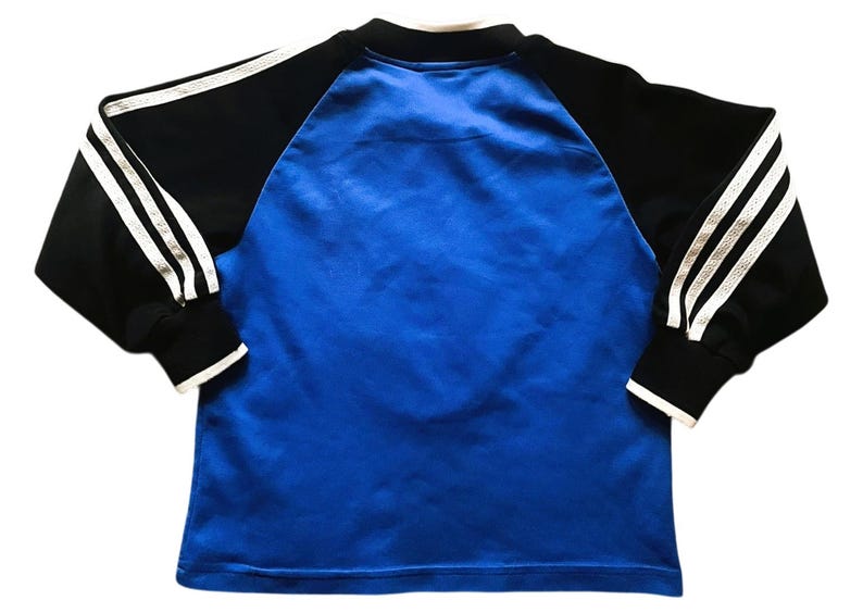 K&ouml;nnte beinhalten: Ein blau-schwarzes Langarmshirt. Das Shirt hat einen blauen K&ouml;rper mit schwarzen &Auml;rmeln. Die &Auml;rmel haben drei wei&szlig;e Streifen entlang der Arml&auml;nge. Die Manschetten und der Kragen sind wei&szlig; eingefasst.