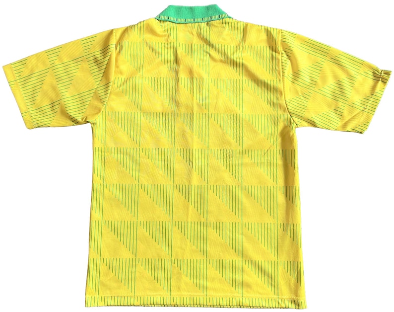 K&ouml;nnte beinhalten: Ein gelbes Fu&szlig;balltrikot mit kurzen &Auml;rmeln, gr&uuml;nem Kragen und einem geometrischen Muster aus d&uuml;nnen gr&uuml;nen Linien.