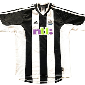 May include: A white and black striped football shirt with a black collar and short sleeves. The shirt has the Adidas logo on the left breast and the NTL logo on the front. The Newcastle United crest is on the right breast.