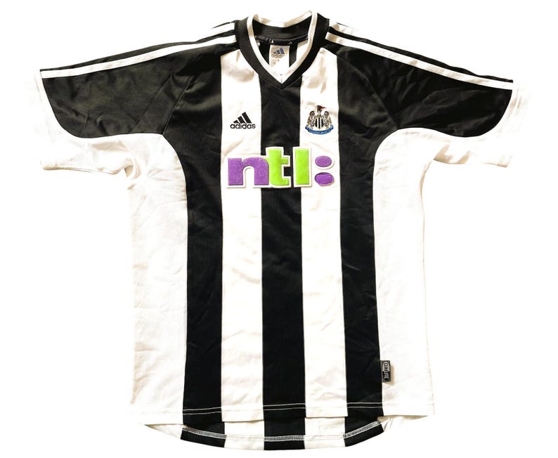 May include: A white and black striped football shirt with a black collar and short sleeves. The shirt has the Adidas logo on the left breast and the NTL logo on the front. The Newcastle United crest is on the right breast.