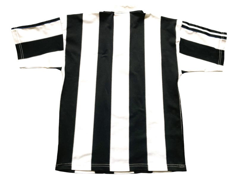 May include: Black and white striped jersey. The shirt has a classic design with vertical black stripes alternating with white stripes. The sleeves have black and white striped cuffs. The collar is white.