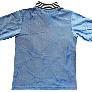 May include: A short-sleeved blue shirt with a ribbed collar featuring black and white stripes. The shirt is made of a shiny, textured fabric. The garment is laid flat, showcasing the back of the shirt.