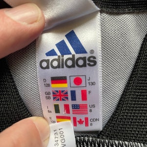 May include: White tag with black adidas logo and size chart in various languages and measurements. The tag also includes the numbers 634731 and AVG001.