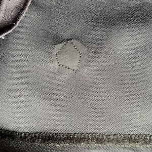 May include: Close-up of dark gray fabric with a pentagon-shaped patch stitched on. The patch is the same color as the fabric. The image shows the texture of the material and the stitching detail.