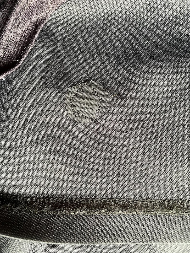 May include: Close-up of dark gray fabric with a pentagon-shaped patch stitched on. The patch is the same color as the fabric. The image shows the texture of the material and the stitching detail.