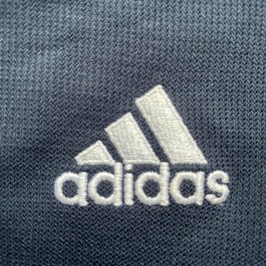 Puede incluir: Primer plano de una tela azul marino con un logotipo de Adidas bordado en blanco.