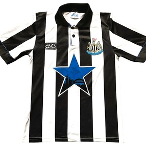 May include: Black and white striped soccer jersey with a blue star graphic. The jersey has a collar and short sleeves. The Asics logo is visible on the chest. The Newcastle United crest is on the chest.