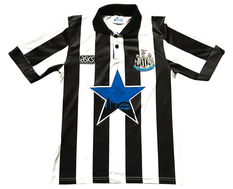May include: Black and white striped soccer jersey with a blue star graphic. The jersey has a collar and short sleeves. The Asics logo is visible on the chest. The Newcastle United crest is on the chest.