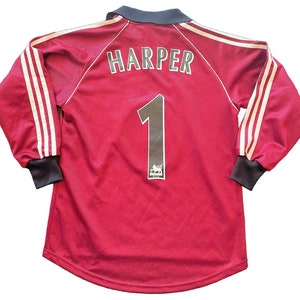 May include: Maroon long-sleeved jersey with white stripes on the sleeves. The name "HARPER" is printed across the upper back, with the number "1" below. A logo is visible below the number. The collar and cuffs are dark navy.