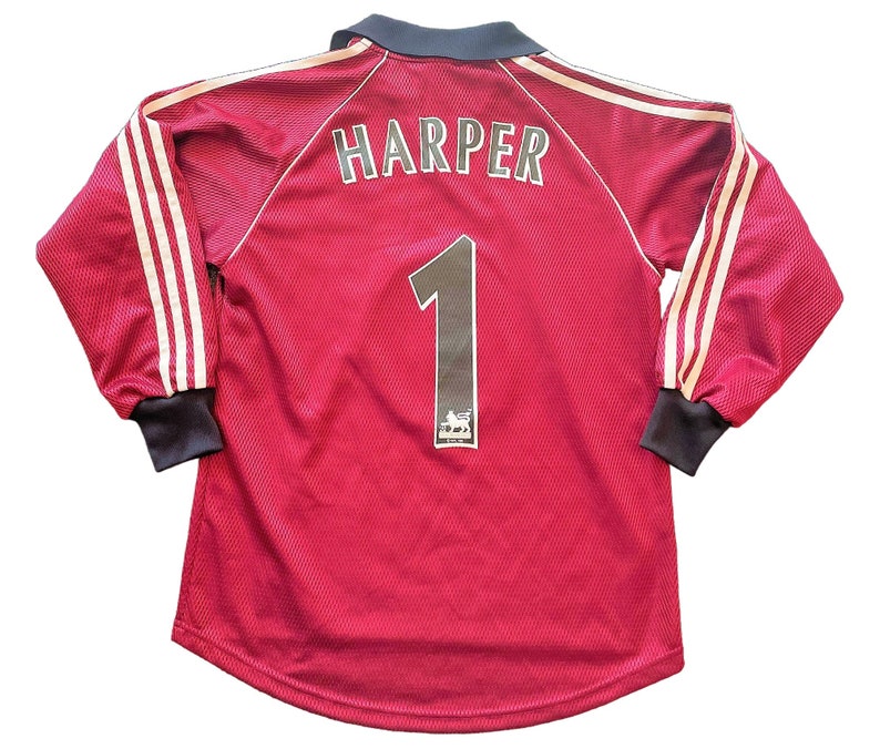 May include: Maroon long-sleeved jersey with white stripes on the sleeves. The name "HARPER" is printed across the upper back, with the number "1" below. A logo is visible below the number. The collar and cuffs are dark navy.