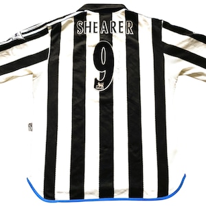 Puede incluir: Camiseta de f&uacute;tbol a rayas blancas y negras con ribetes azules. La parte posterior de la camiseta tiene el nombre "SHERER" y el n&uacute;mero "9" impreso.