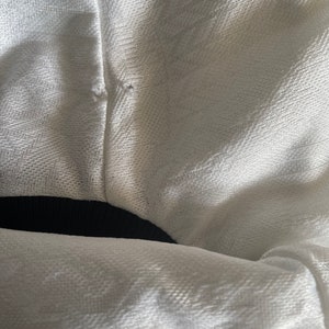 May include: White fabric with a black waistband. The fabric has a textured weave.
