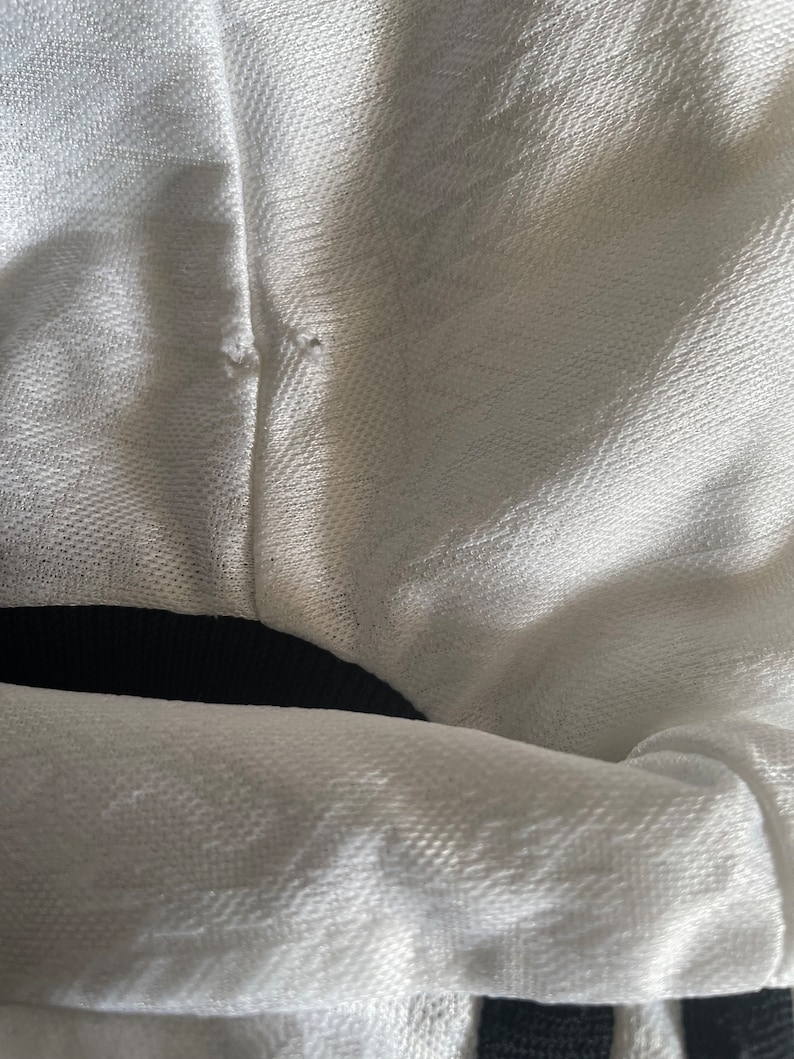 May include: White fabric with a black waistband. The fabric has a textured weave.