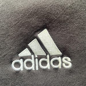 May include: A white embroidered Adidas logo on a black fabric background.