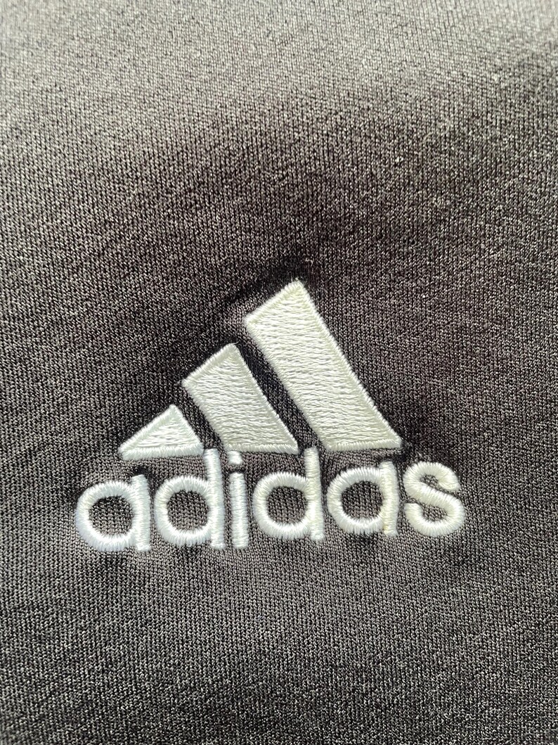 May include: A white embroidered Adidas logo on a black fabric background.