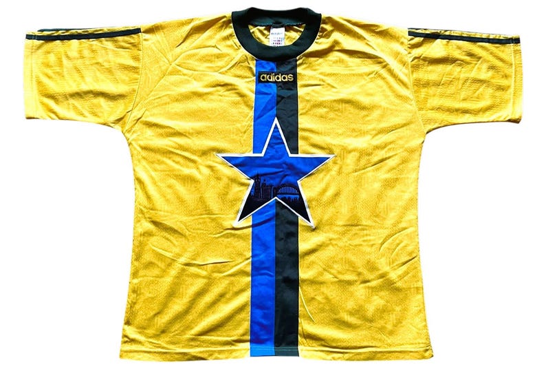 May include: A yellow soccer jersey with a blue and black star design on the front. The jersey has a blue stripe down the center and the Adidas logo at the top. The sleeves have black stripes.