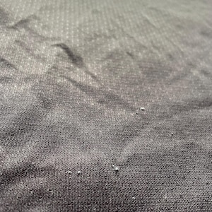 May include: Close-up of a black athletic shirt with a red design. The fabric has a textured, dotted pattern. The shirt appears to be made of a breathable material, suitable for sports or workouts.