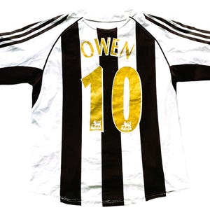 May include: A white and black striped soccer jersey with gold lettering. The name "OWEN" and the number "10" are on the back of the jersey.