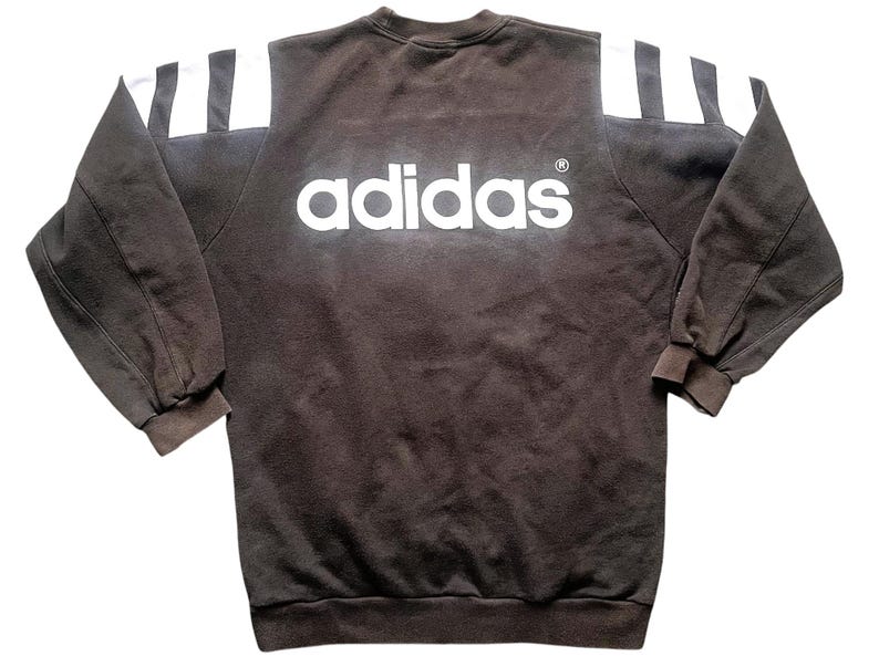 May include: A brown sweatshirt with white stripes on the shoulders and the word "adidas" in white letters on the front.