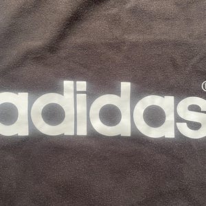 May include: White adidas logo on a dark brown background with a registered trademark symbol.