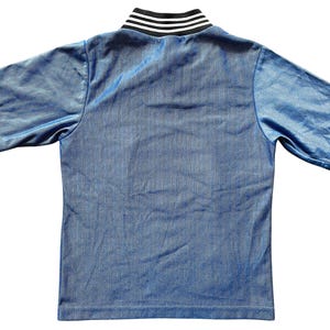 May include: A short-sleeved, light blue shirt with a ribbed texture. The collar is a contrasting black and white striped design. The shirt is made of a shiny, athletic material.
