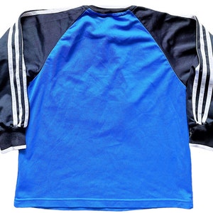 May include: A blue long-sleeve shirt with black and white striped sleeves. The shirt has a raglan design and a crew neck.