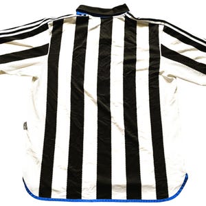 May include: A black and white striped soccer jersey with blue trim. The jersey has a collar and short sleeves.