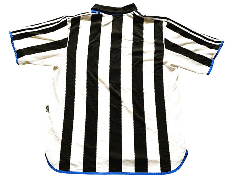 May include: A black and white striped soccer jersey with blue trim. The jersey has a collar and short sleeves.