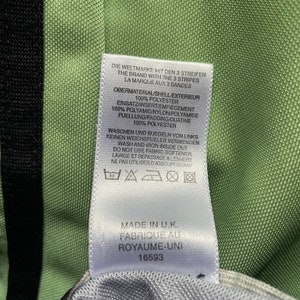 May include: Close-up of a tag with text in multiple languages, including English, French, and German. The tag is white with black text and is attached to a green and black fabric. The tag indicates the item was made in the U.K.