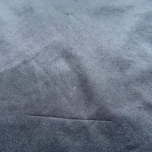 May include: Close-up of a black fabric with a subtle texture. The fabric has a seam running horizontally across the bottom of the image.