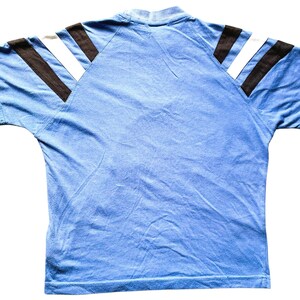 May include: A light blue short-sleeved t-shirt with black and white stripes on the shoulders.