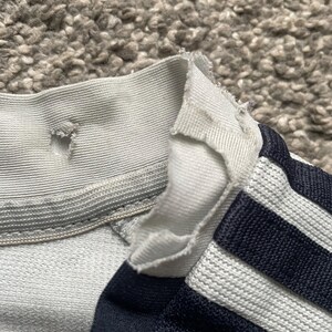 Puede incluir: Una camisa a rayas blancas y azul marino con el cuello roto. La camisa tiene un cuello acanalado blanco y una raya blanca en cada manga.