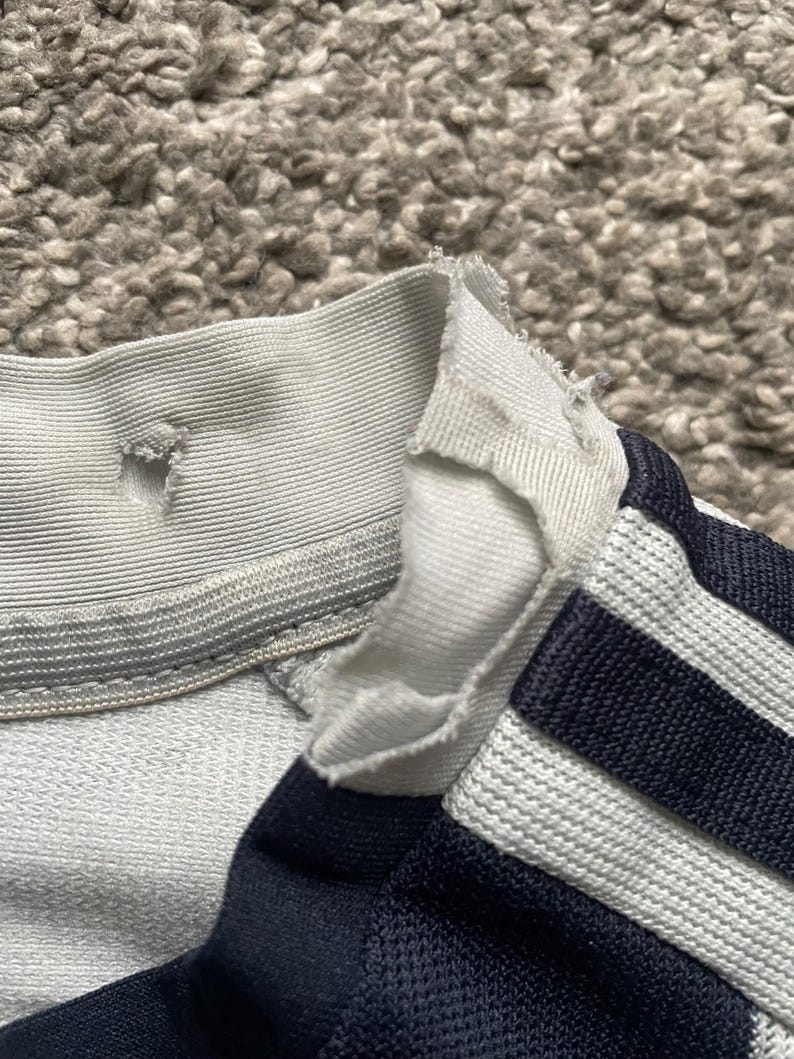 Puede incluir: Una camisa a rayas blancas y azul marino con el cuello roto. La camisa tiene un cuello acanalado blanco y una raya blanca en cada manga.