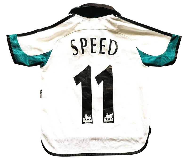 Puede incluir: Camiseta de f&uacute;tbol blanca con detalles en negro, que muestra el nombre "SPEED" y el n&uacute;mero "11" en negro. La camiseta tiene detalles de malla verde azulado en las mangas y un cuello negro. El logotipo de la Premier League es visible.