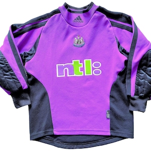 May include: Purple and black long-sleeved soccer jersey with the Adidas logo, the Newcastle United crest, and the NTL logo. The jersey has black padding on the elbows.