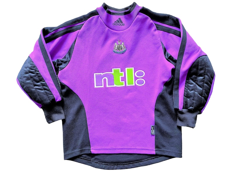 May include: Purple and black long-sleeved soccer jersey with the Adidas logo, the Newcastle United crest, and the NTL logo. The jersey has black padding on the elbows.