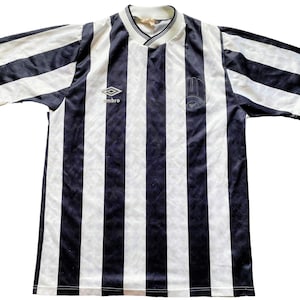 May include: Black and white striped soccer jersey with the logo "Umbro" and a team logo on the front.
