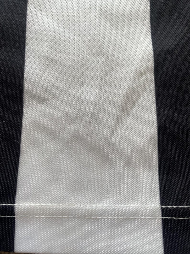 May include: Close-up of a fabric with a vertical black and white striped pattern. The white stripe has a textured appearance, and a seam runs horizontally across the bottom of the image.