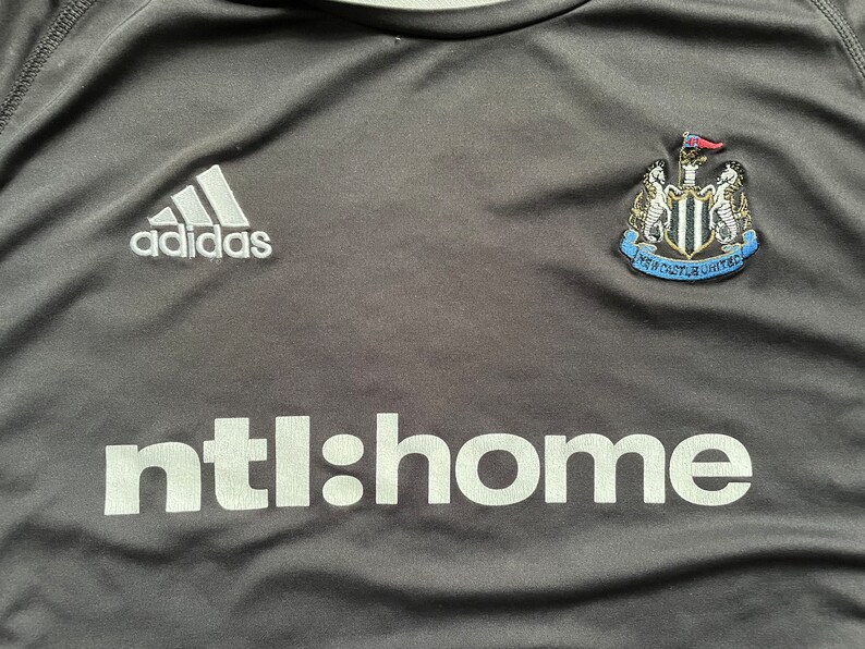 May include: Black soccer jersey with white Adidas logo, Newcastle United crest, and "ntl:home" text.