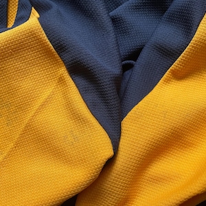 May include: Close-up of a yellow and navy blue fabric with a textured pattern. The fabric is folded in half, showing the two different colors.