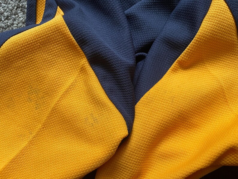 May include: Close-up of a yellow and navy blue fabric with a textured pattern. The fabric is folded in half, showing the two different colors.