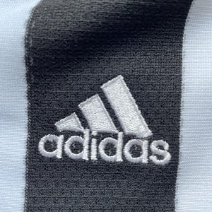 Pode incluir: Um tecido listrado branco e preto com um logotipo Adidas branco bordado em uma faixa preta.