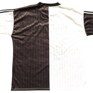 May include: A two-tone sports jersey, split vertically with a dark brown and white design. The jersey has a black collar and sleeve cuffs with white stripes. The fabric has a subtle ribbed texture.