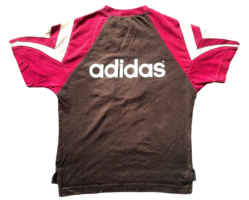 Puede incluir: Una camiseta Adidas marr&oacute;n con detalles burdeos y blancos. El logotipo de Adidas en blanco est&aacute; en el pecho. Las mangas tienen rayas blancas y paneles burdeos.