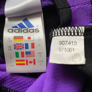 May include: A white tag with the adidas logo and size information in multiple languages and measurements. The tag also includes the numbers 907415 and 971001.