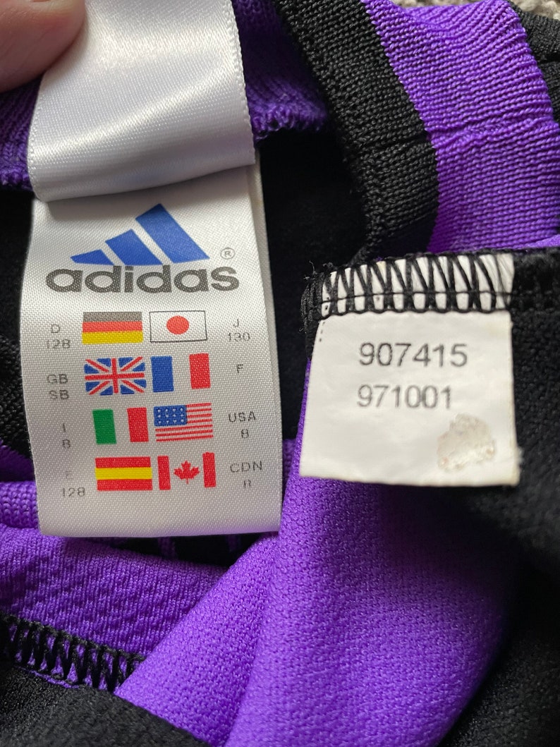 May include: A white tag with the adidas logo and size information in multiple languages and measurements. The tag also includes the numbers 907415 and 971001.
