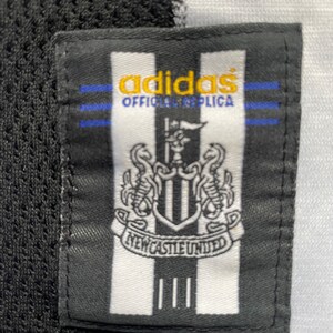 May include: Black and white adidas football shirt patch with the Newcastle United crest and the text "adidas Official Replica".